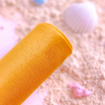 Rolo mostarda aveludado sobre areia com pequenas conchas coloridas