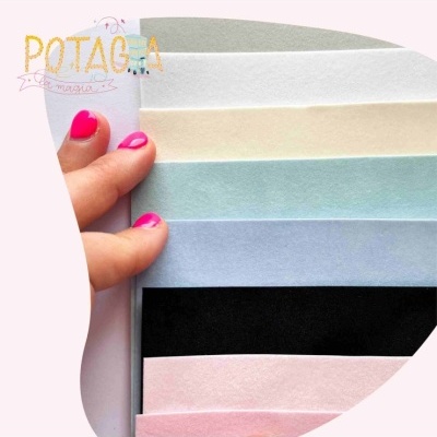 Folhas de papel coloridas em tons pastel e preto, seguradas por mão com unhas rosa, logo POTAG.A MAGIA ao fundo