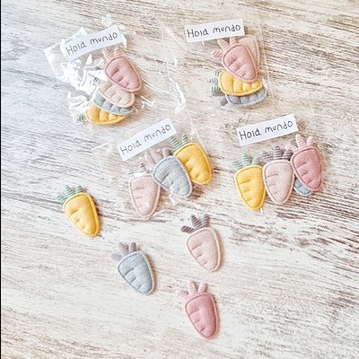 Aplicações de tecido em forma de cenoura em rosa, cinza e amarelo embaladas em plástico transparente com etiquetas