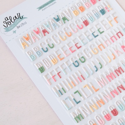 Folha de autocolantes de letras coloridas com glitter em embalagem branca sobre mesa de madeira clara