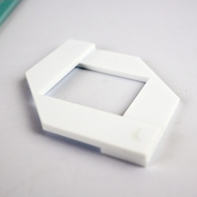 Peça plástica branca hexagonal com abertura retangular sobre superfície branca