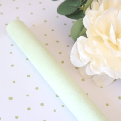 Rolo branco esponjoso junto a flor branca artificial sobre papel com padrão de pontos dourados