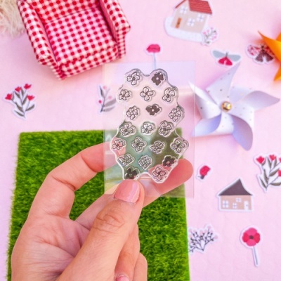 Mão a segurar folha transparente com autocolantes de flores pretas e brancas sobre fundo rosa decorado.