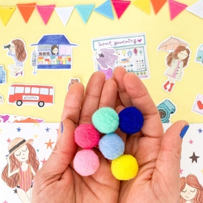 Mãos segurando pompons de lã coloridos com fundo ilustrado amarelo