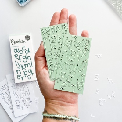 Mão segurando placas verdes com letras em relevo e caixas de botões coloridos ao fundo