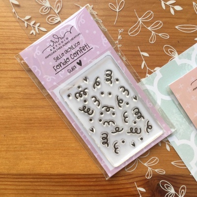 Selo acrílico com motivos de confetes em embalagem rosa sobre mesa de madeira