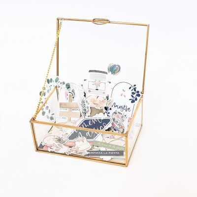 Caixa transparente de vidro com moldura dourada e recortes decorativos coloridos com textos em espanhol