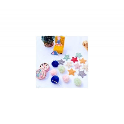 Enfeites de estrelas de tecido e pompons de lã coloridos sobre superfície branca com caixa, cacto e fita colorida.