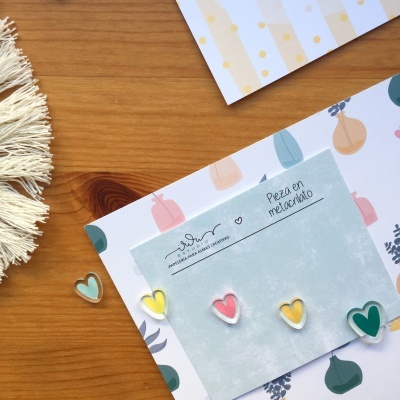 Cinco pins em forma de coração coloridos sobre cartão azul claro e mesa de madeira