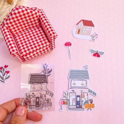 Mini poltrona xadrez vermelho e branco com autocolantes de casas e flores sobre fundo rosa.