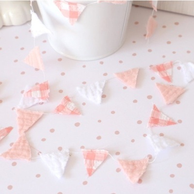 Cordão decorativo de tecido com bandeirinhas triangulares rosa e branco sobre superfície com bolinhas