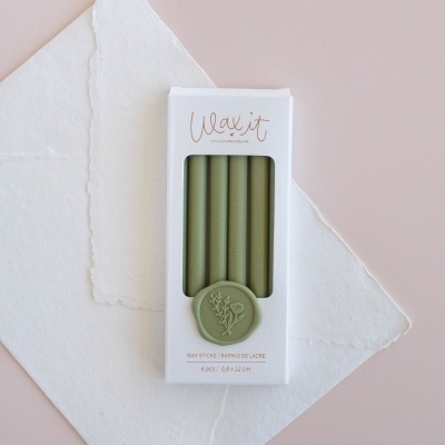 Caixa de velas verdes Wax it com selo decorativo, sobre papel branco e fundo rosa.