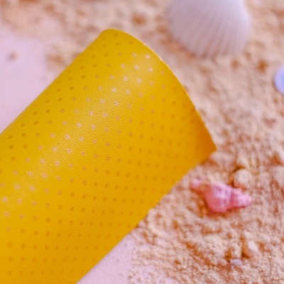 Rolo de silicone amarelo com textura pontilhada e conchas coloridas sobre areia e superfície clara