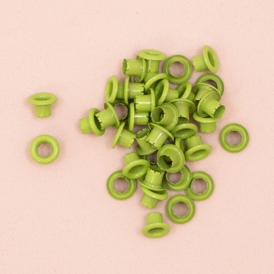 Ilhós verdes com anel metálico sobre superfície rosa