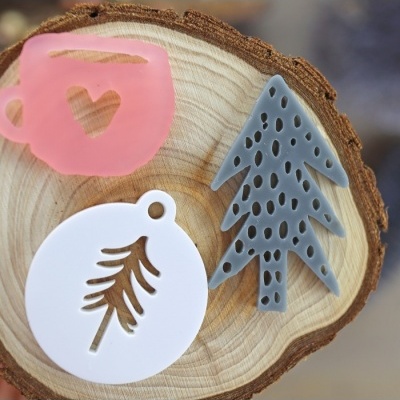 Moldes de silicone em forma de copo, árvore e círculo com ramo, sobre um corte transversal de madeira.