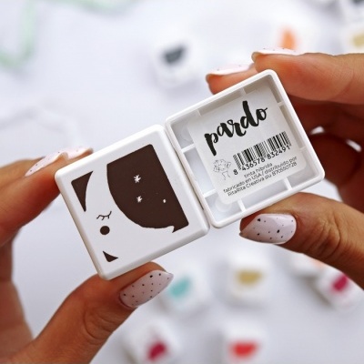 Caixa branca com carimbo de face e lua e etiqueta 'pardo' segurada por mãos com unhas pintadas