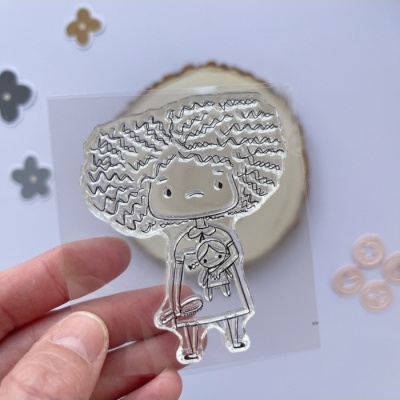 Carimbo transparente de menina com cabelo encaracolado a segurar uma boneca