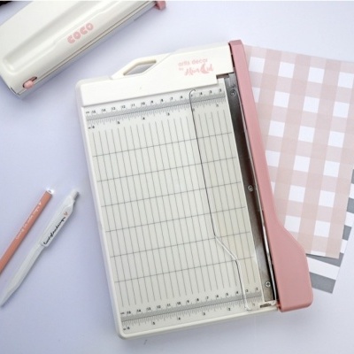 Guilhotina de papel branca e rosa com canetas e blocos de papel xadrez