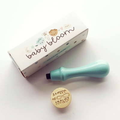 Selo de madeira com cabo azul claro e caixa branca com texto baby bloom