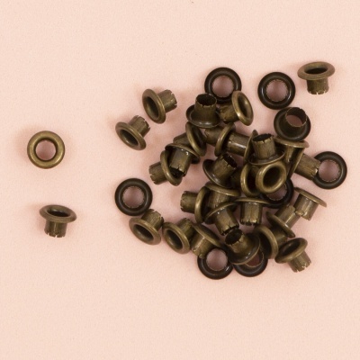 Ilhós metálicos bronze com anéis pretos sobre fundo rosa claro