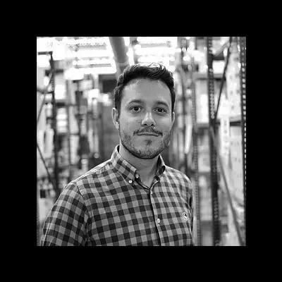 Homem com camisa quadriculada em ambiente industrial com estantes ao fundo