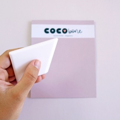 Pessoa segurando objeto branco triangular com fundo lilás e texto COCO bone