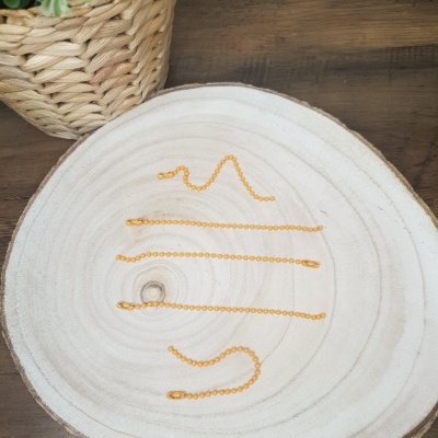 Quatro correntes douradas finas sobre tábua de madeira clara com vaso de planta ao fundo