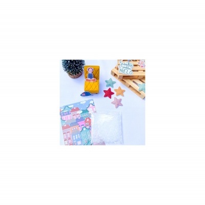 Caixa amarela com boneca, estrelas de tecido coloridas, saco com pérolas, embalagem ilustrada, vaso com cacto e placa de madeira com texto.