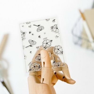 Cartão branco com flores e abelhas a preto segurado por mão de madeira