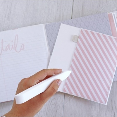 Mão segurando caneta branca sobre caderno aberto com páginas em rosa e branco