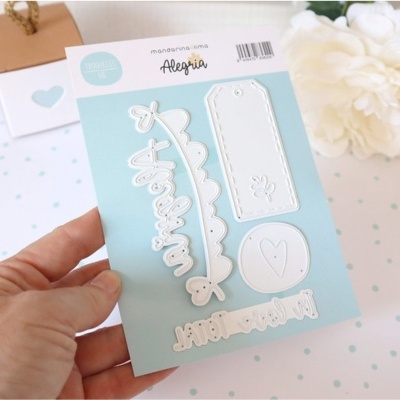 Conjunto de cortes metálicos para scrapbooking montados em cartolina azul clara com texto, mão segurando e fundo branco com padrão azul e flor branca