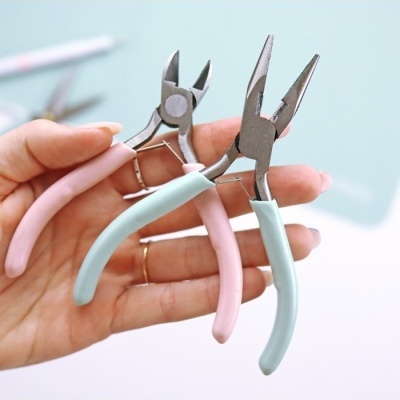 Três alicates com punhos coloridos em azul e rosa segurados por uma mão