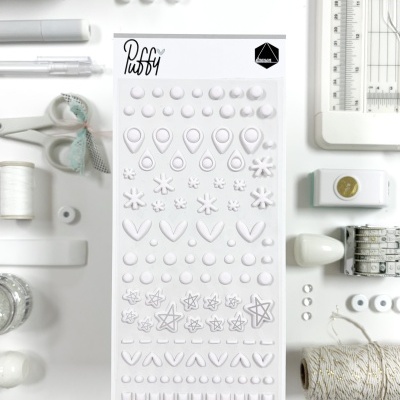 Folha de autocolantes em relevo branco com diversas formas, rodeada por material de escritório e artesanato