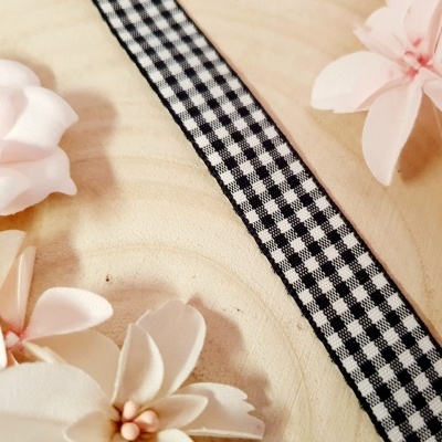 Fita decorativa preta e branca com padrão vichy sobre madeira clara com flores artificiais ao redor.
