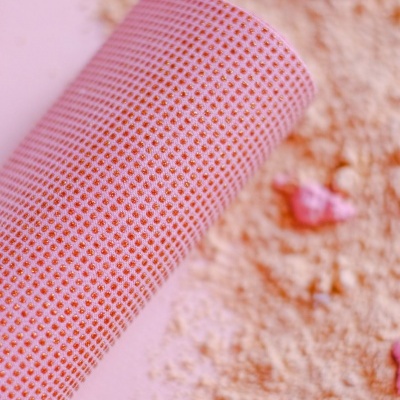 Rolo de tecido cor de rosa com pontos vermelhos sobre superfície rosa com areia e conchas