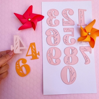 Números decorativos de papel em cores rosa e laranja com cataventos coloridos sobre superfície rosa