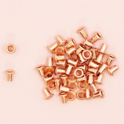 Ilhós metálicos cor cobre sobre fundo rosa pálido