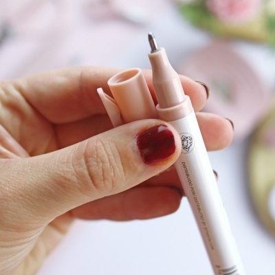 Mão a segurar caneta bege e branca com ponta de feltro fina e tampa removida