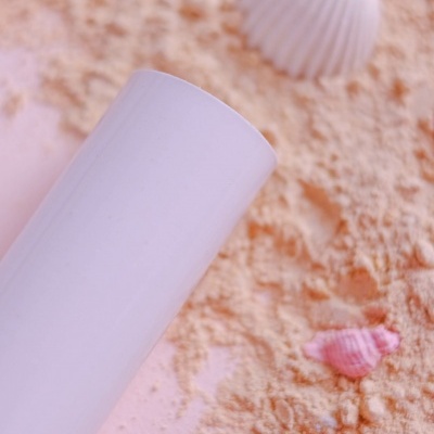 Cilindro branco sobre fundo de areia com conchas coloridas