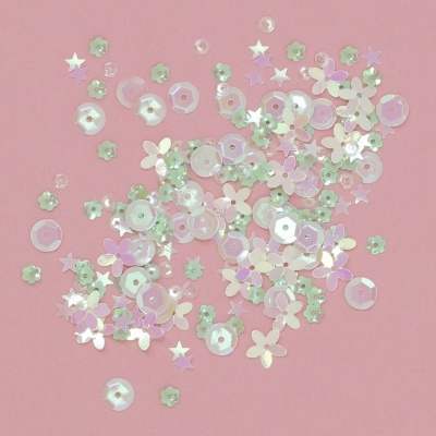 Conjunto de lantejoulas coloridas e brilhantes em forma de estrelas, flores e hexágonos, sobre fundo rosa.