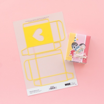 Molde amarelo para caixa com coração e caixa colorida montada sobre fundo rosa