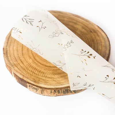 Rolo de papel translúcido com padrão floral dourado sobre placa de madeira