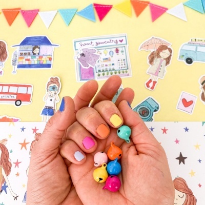 Mãos seguram pequenos acessórios coloridos em forma de baleia com fundo de desenhos e bandeirolas