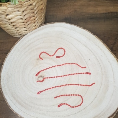 Colar com corrente de pequenas contas vermelhas sobre disco decorativo branco e vaso de plantas em fibra natural