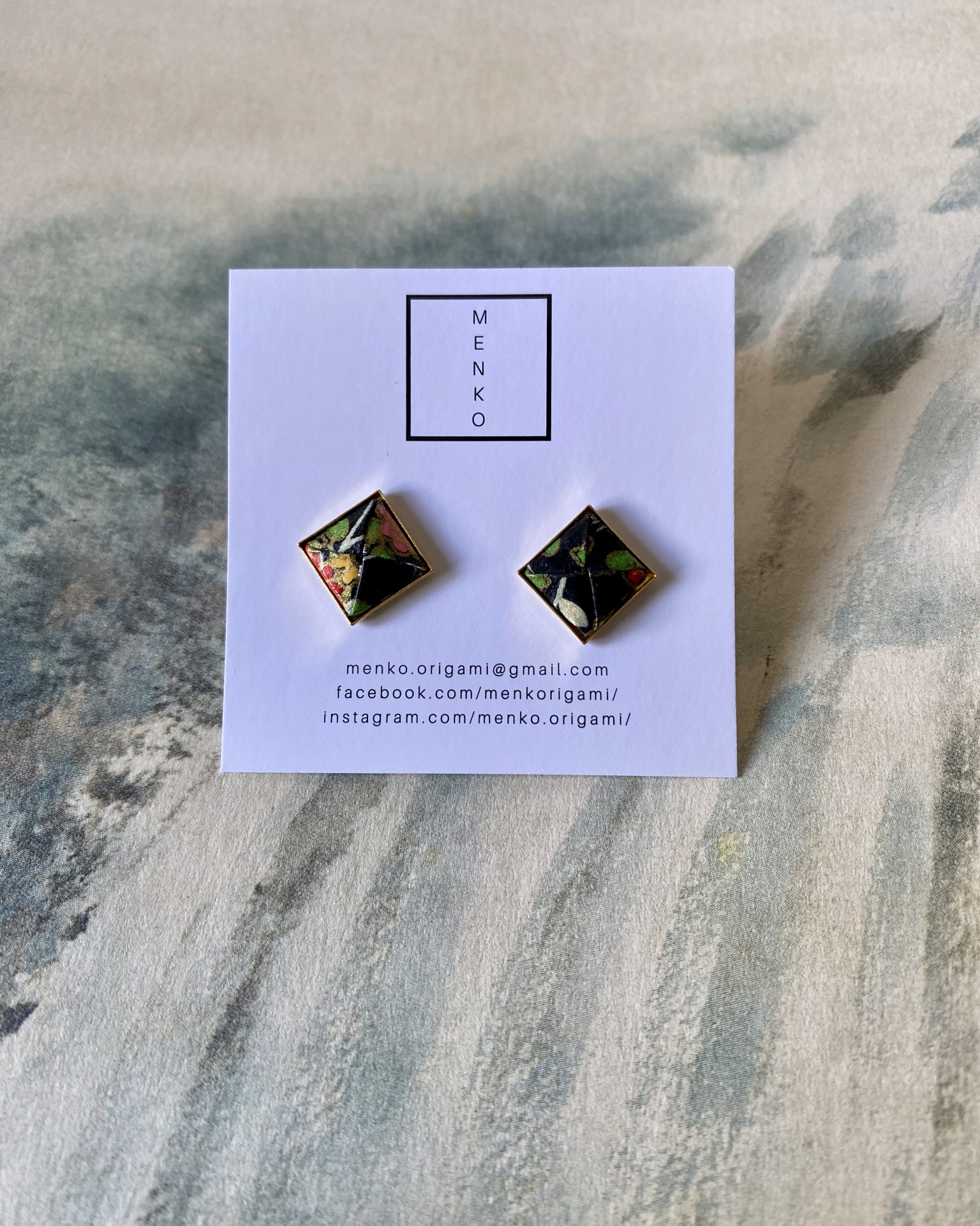 Brincos Menko Clássico Brincos quadrados com padrão colorido em placa branca MENKO e contatos.