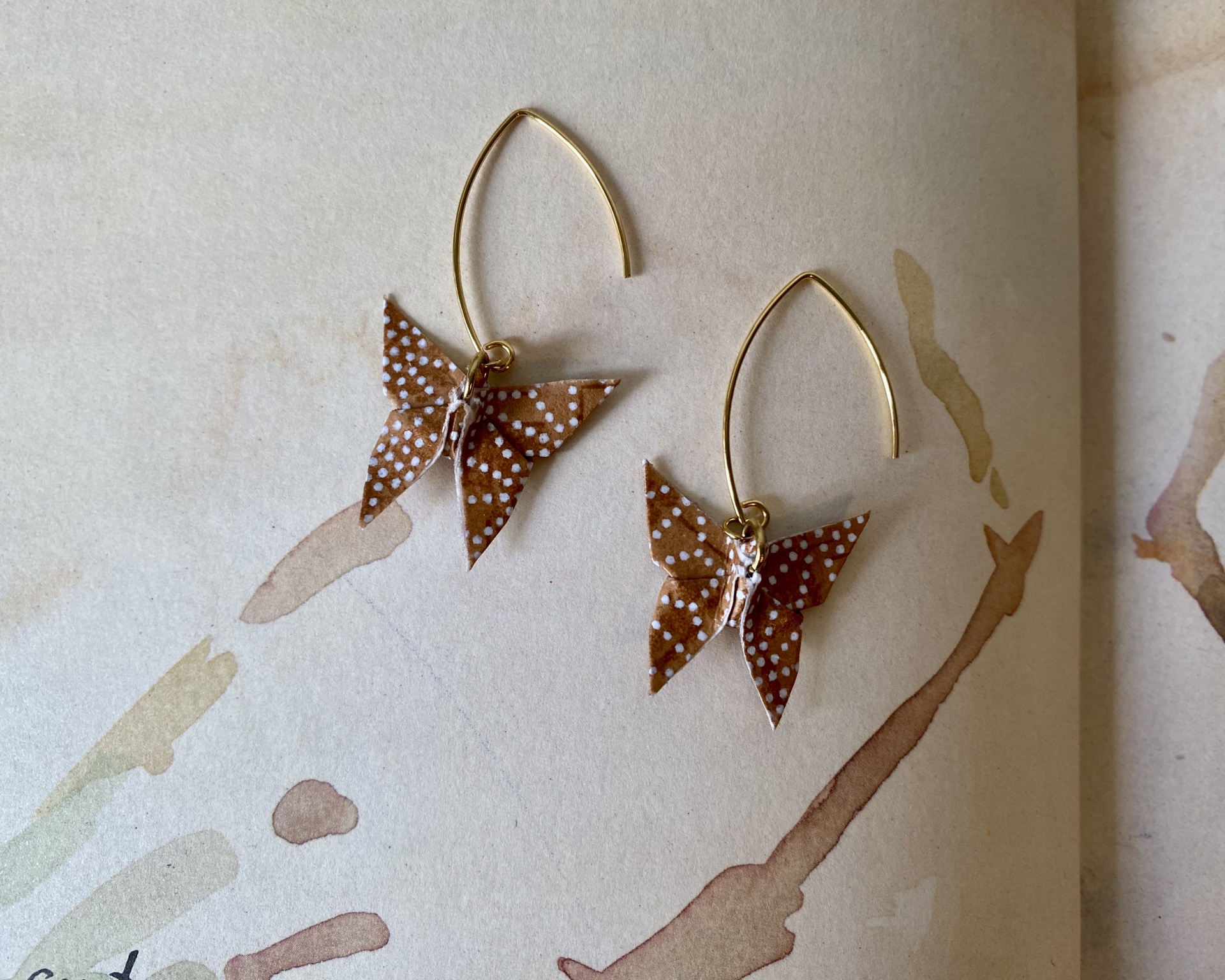 Brincos Borboleta Brincos dourados com borboletas de papel castanho e pontos brancos sobre superfície clara