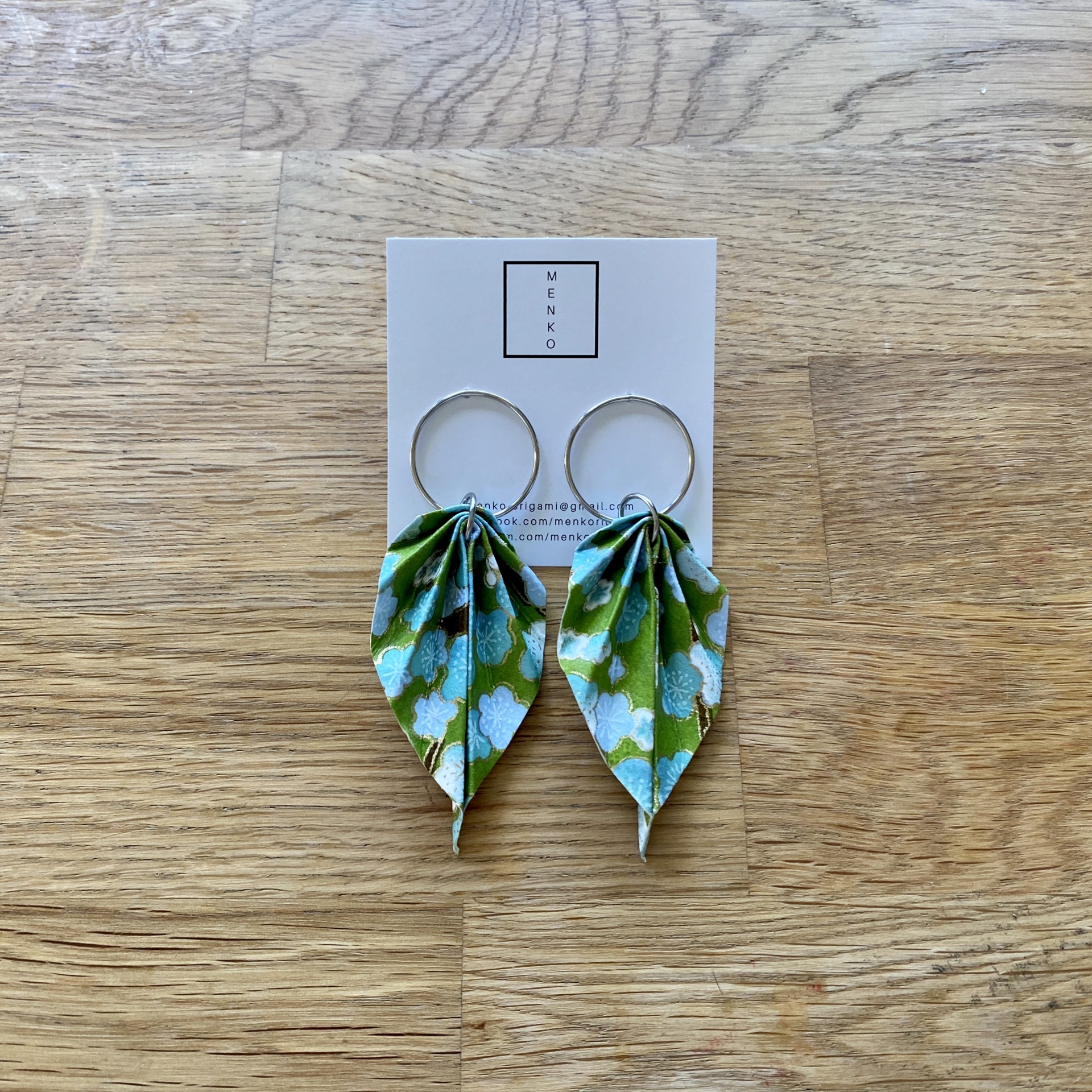 Brincos Folha Brincos com folhas de tecido verde e branco em cartão 'MENKO' sobre madeira clara