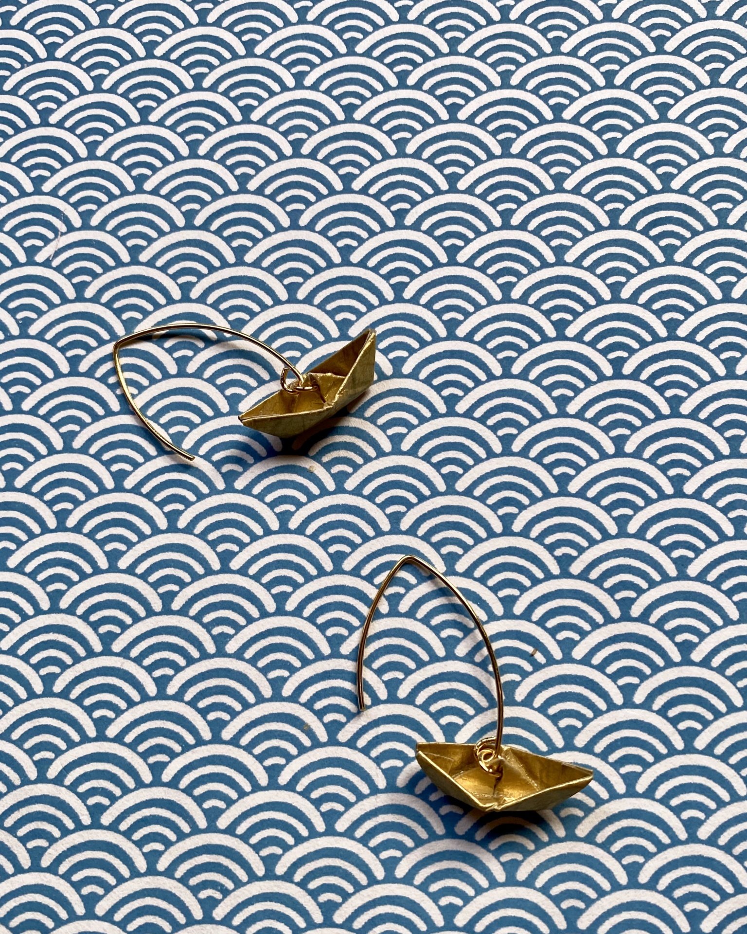 Brincos Boto Brincos dourados em forma de barco sobre fundo azul e branco com padrão de arcos