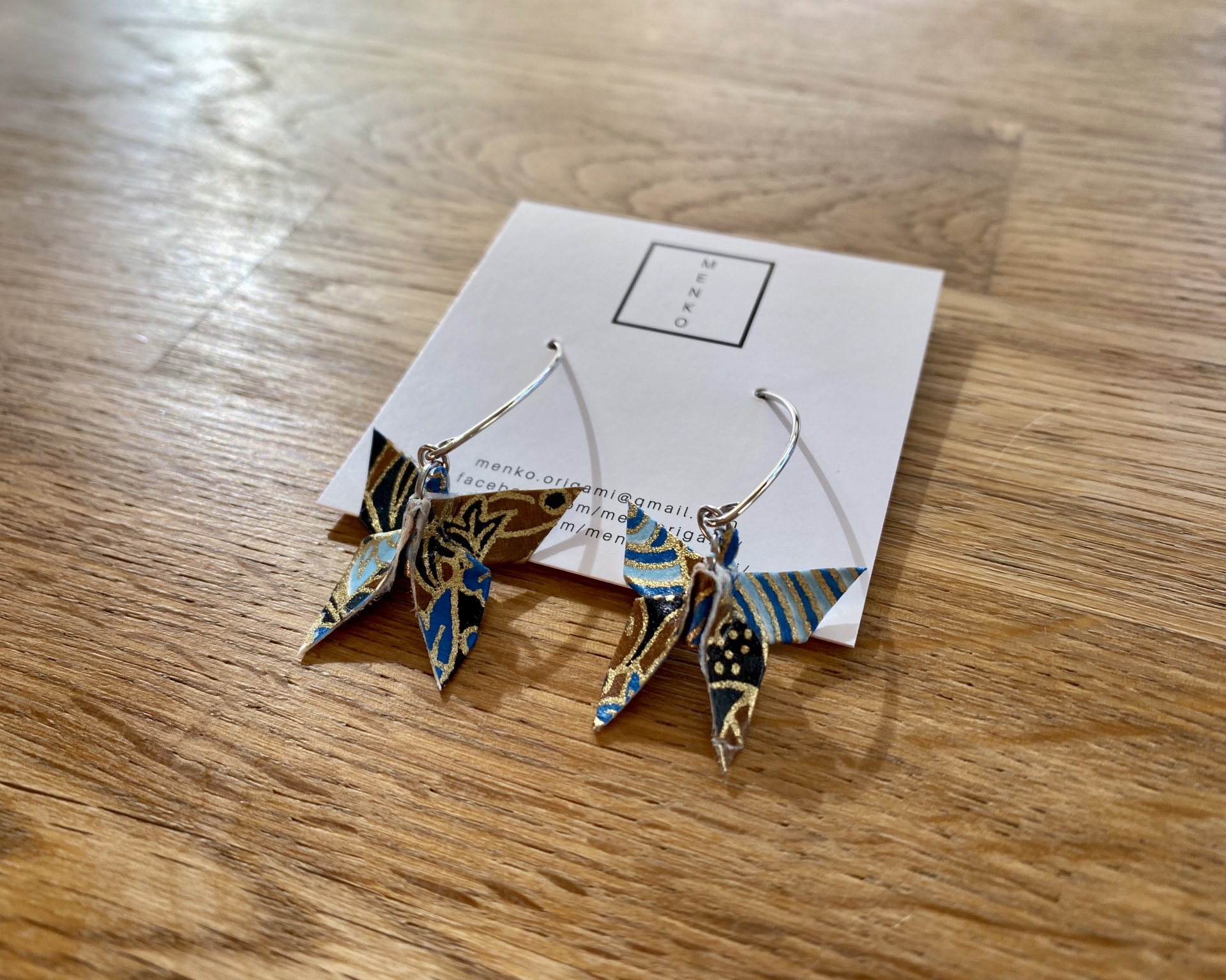 Brincos Borboleta Brincos artesanais de tecido com padrão azul e castanho em cartão branco sobre madeira