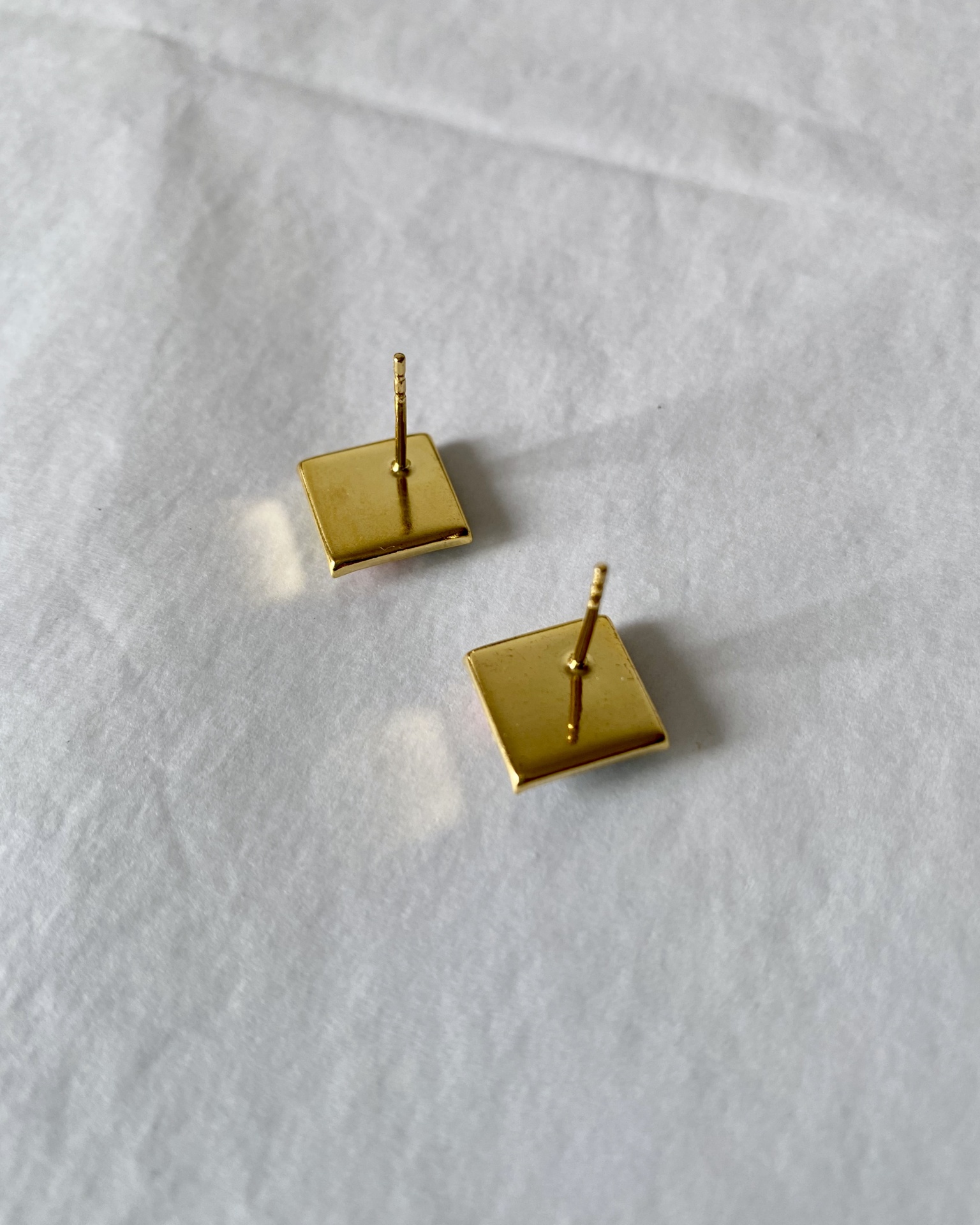 Brincos Menko Clássico Brincos quadrados dourados sobre tecido branco
